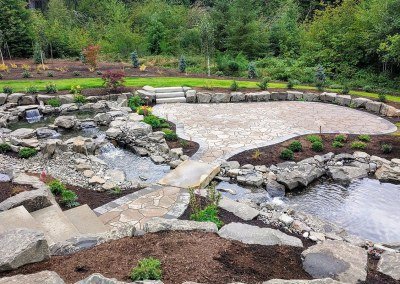 Large Hardscaped Patio with Flowing Mini-Waterfall and Stone Bridge by Dennis' 7 Dees Landscaping