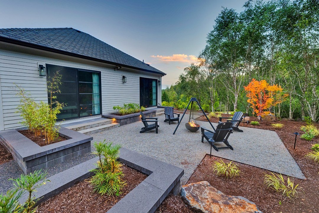 Cauldron fire pit with gravel paths and clean stone walls with plantings - Dennis' 7 Dees Landscaping in Portland A fire pit in a cauldron surrounded by chairs on a gravel square in front of a house - Dennis' 7 Dees Landscaping in Portland