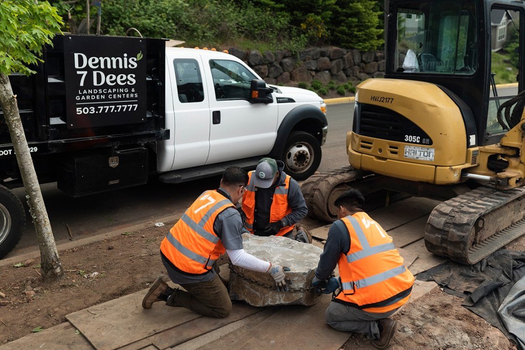 Placing a Boulder in the Landscape - 7 Dees Commercial Landscaping 3 men place a boulder in a landscape surrounded by landscaping equipment - 7 Dees Landscaping