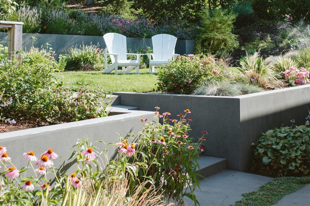 Planter bed retaining wall with 2 white chairs in a summer garden - 7 Dees Landscaping