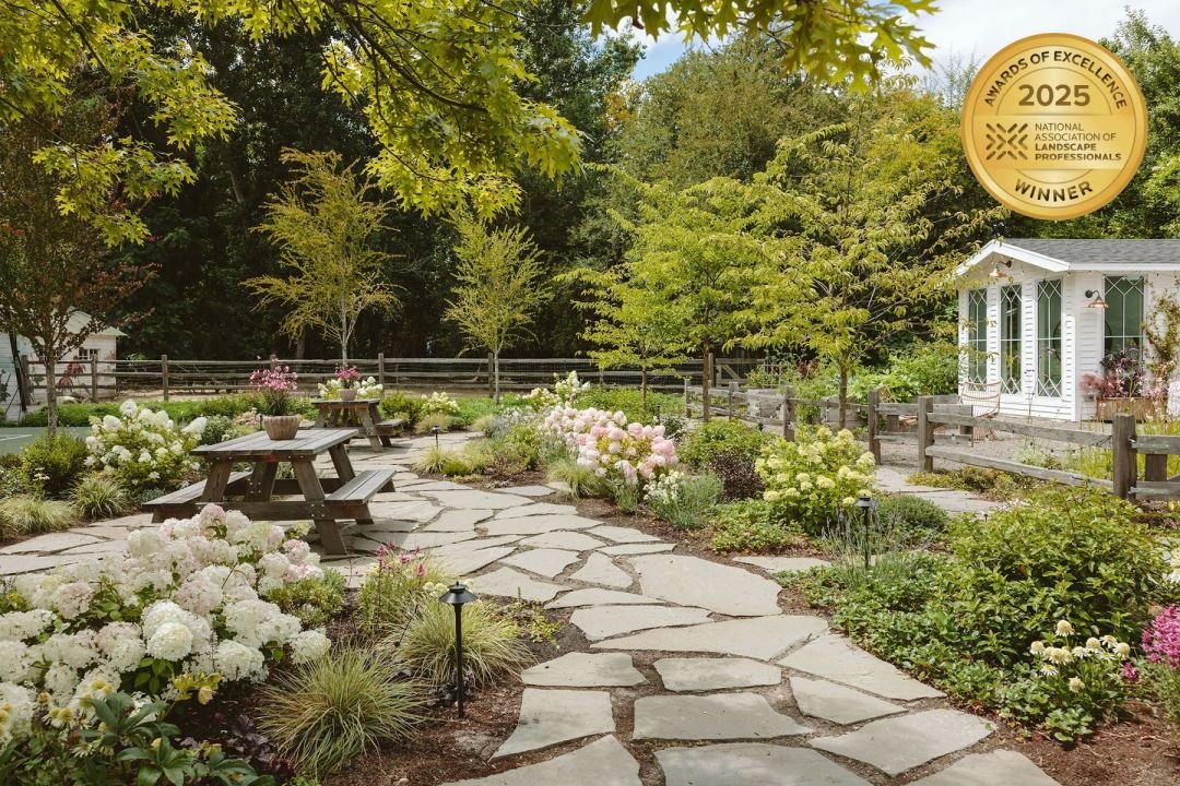 Natural stone paver path through blooming shrubs with picnic tables and a white shed - 7 Dees Landscaping