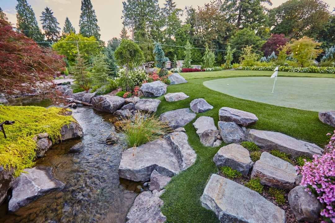 Stream and Putting Green with Boulder - 7 Dees Landscaping Naturalistic manmade stream meanders past boulders and a putting green with trees in the background 7 Dees Landscaping